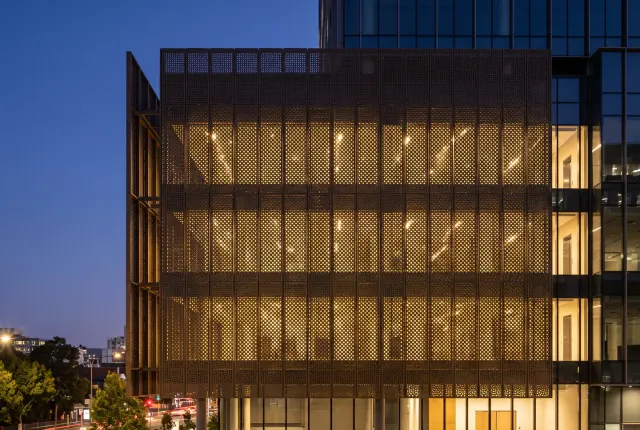 Perforated metal screen facade lit from within at dusk
