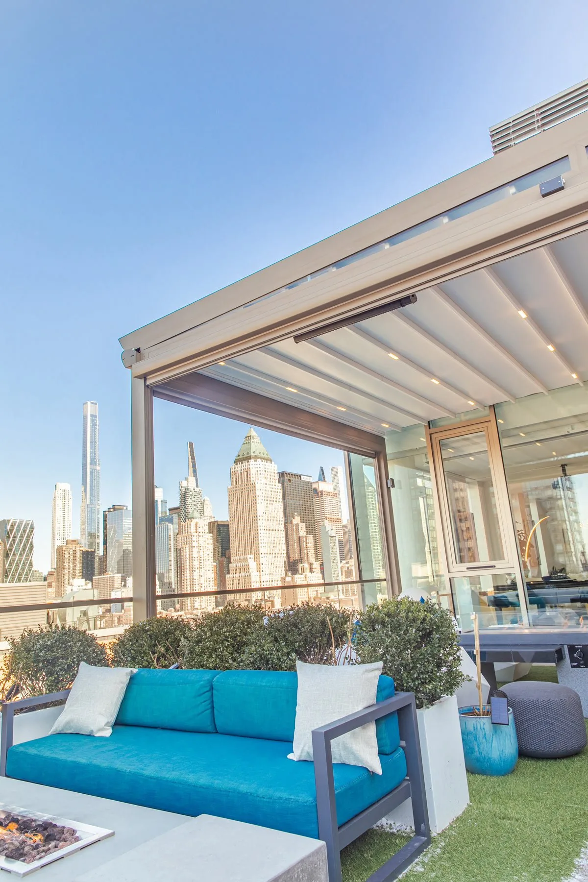 Retractable fabric roof closed over a city roof terrace, ribs running to the frame, tall towers beyond the glazed flank — photograph