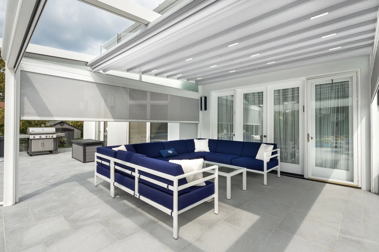 White-framed retractable fabric roof closed over a poolside lounge, pool and loungers beyond the open side — photograph