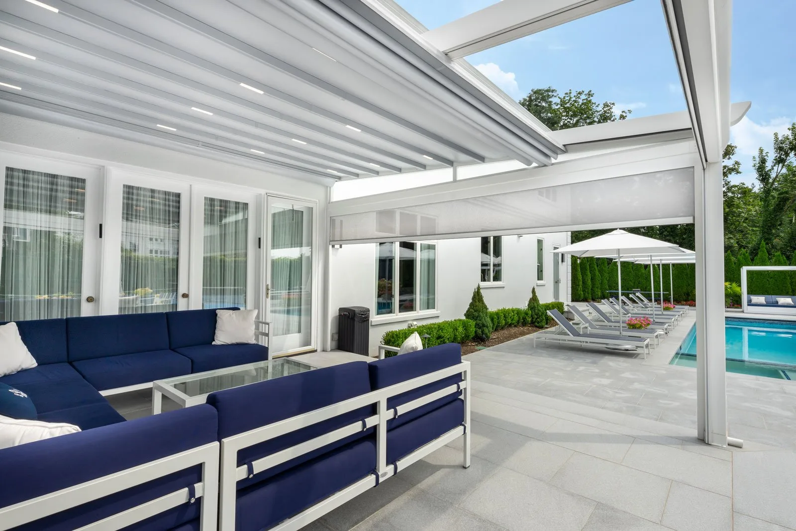 The same white frame with a screen lowered behind the seating group, outdoor kitchen and house doors along the far wall — photograph