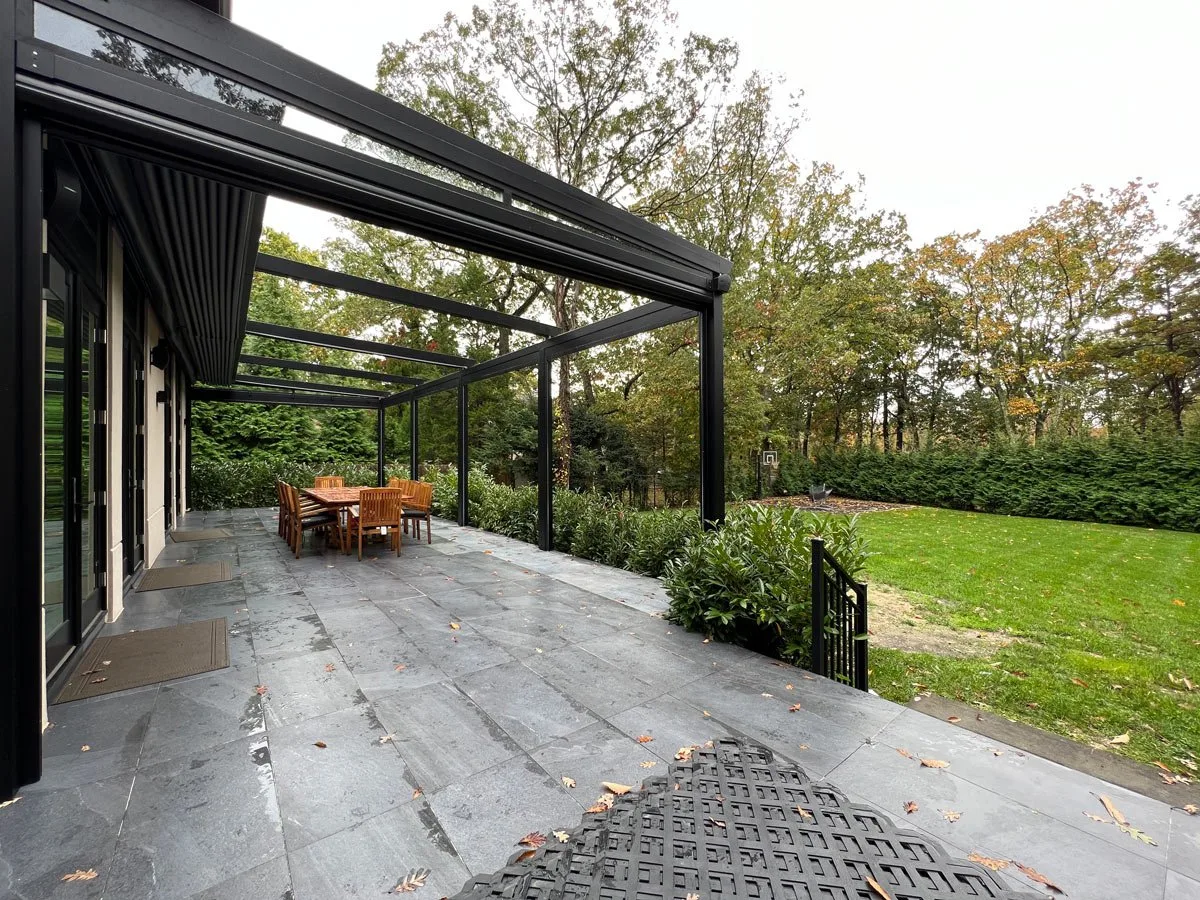 The same patio from the house side, the membrane run out over the dining table and the lawn beyond the open end — photograph