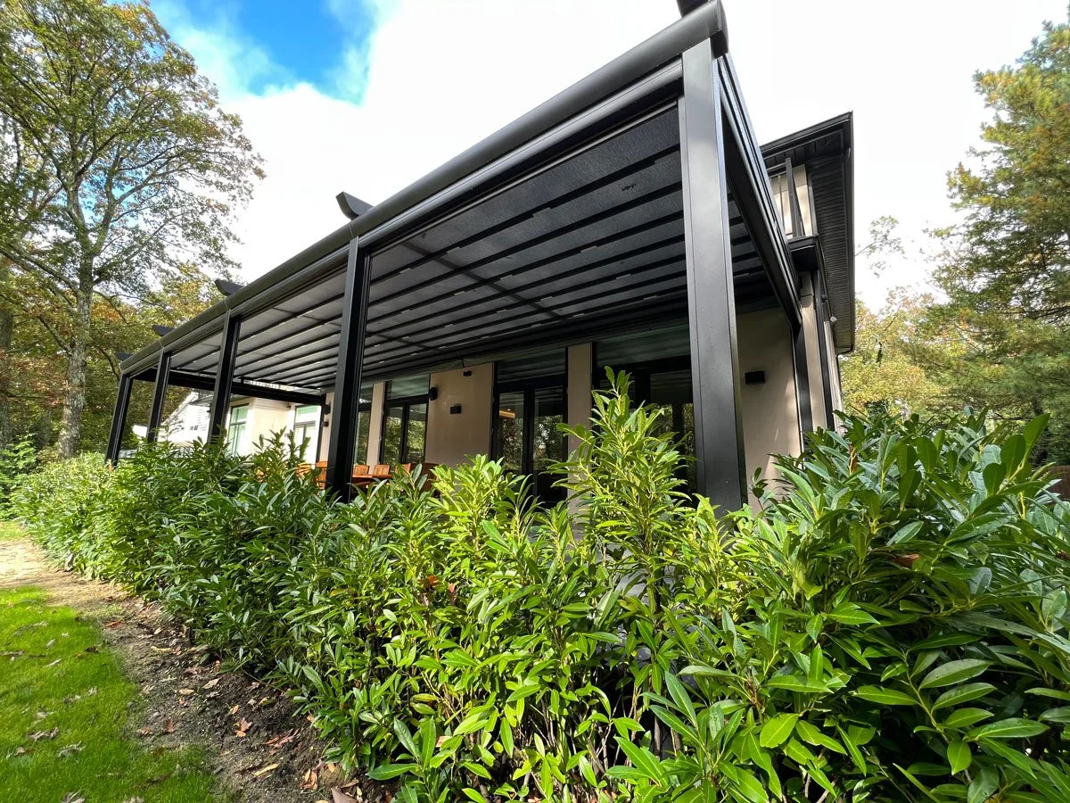 The same structure seen from the garden with the membrane closed across the terrace, hedge and lawn in front — photograph