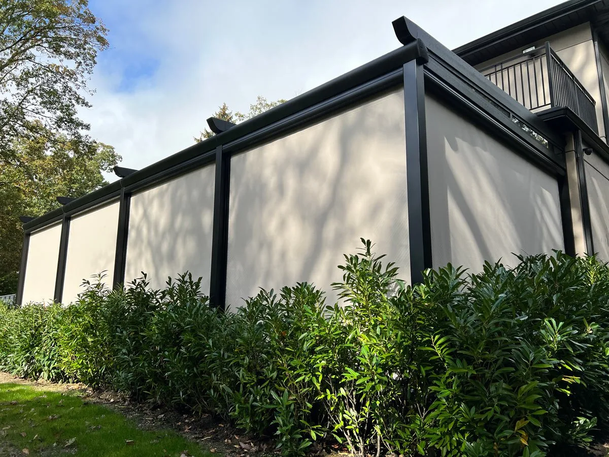 The same structure with screens run down on every side, the terrace closed into a sealed box against the hedge — photograph