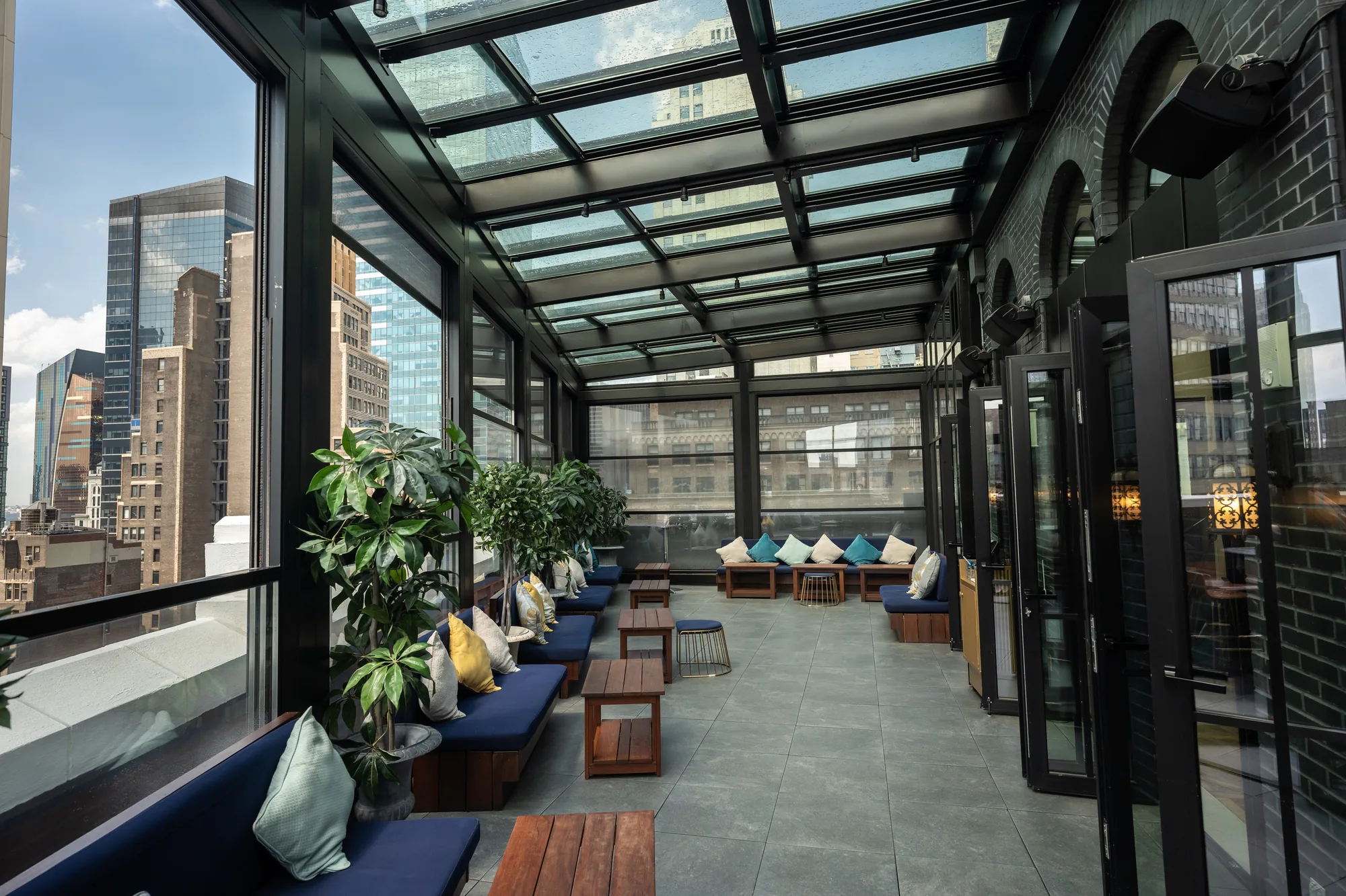 Black-framed glass roof running the length of a rooftop terrace, city towers beyond the glazed side — photograph