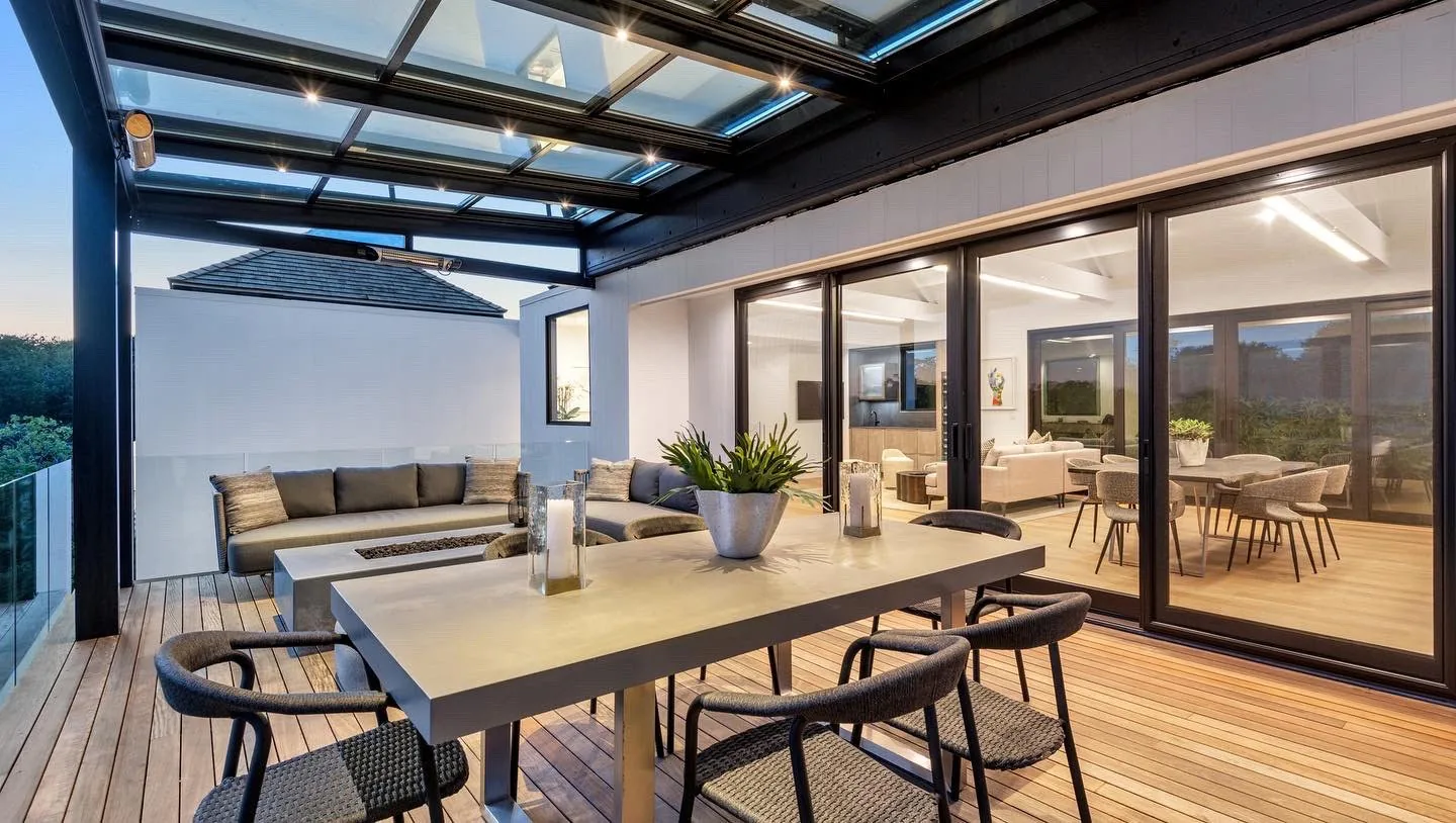 The same terrace from the other end, glass roof over a dining table with sliding doors open into the lit house — photograph