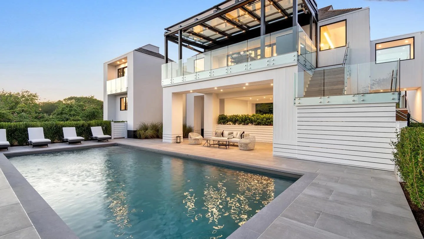 The same house from the pool at dusk, the glass roof visible over the upper terrace above the glass rail — photograph