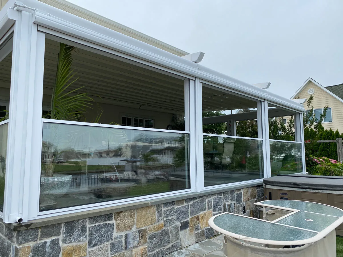 From inside a white-framed enclosure on a stone base, glass panes closed along the water side, a table beneath — photograph