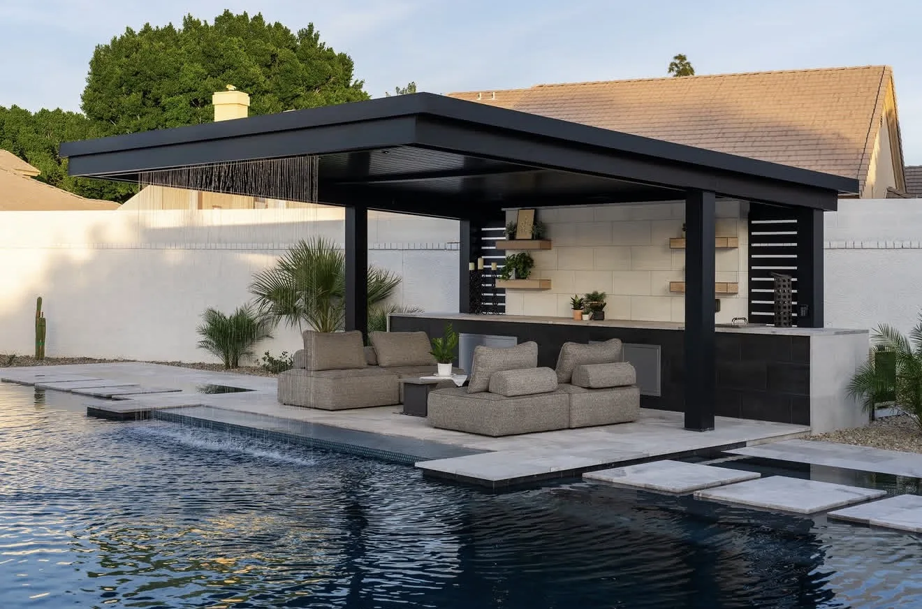 Black-framed hard top pergola at the edge of a pool, solid roof over a built-in kitchen and lounge seating — photograph