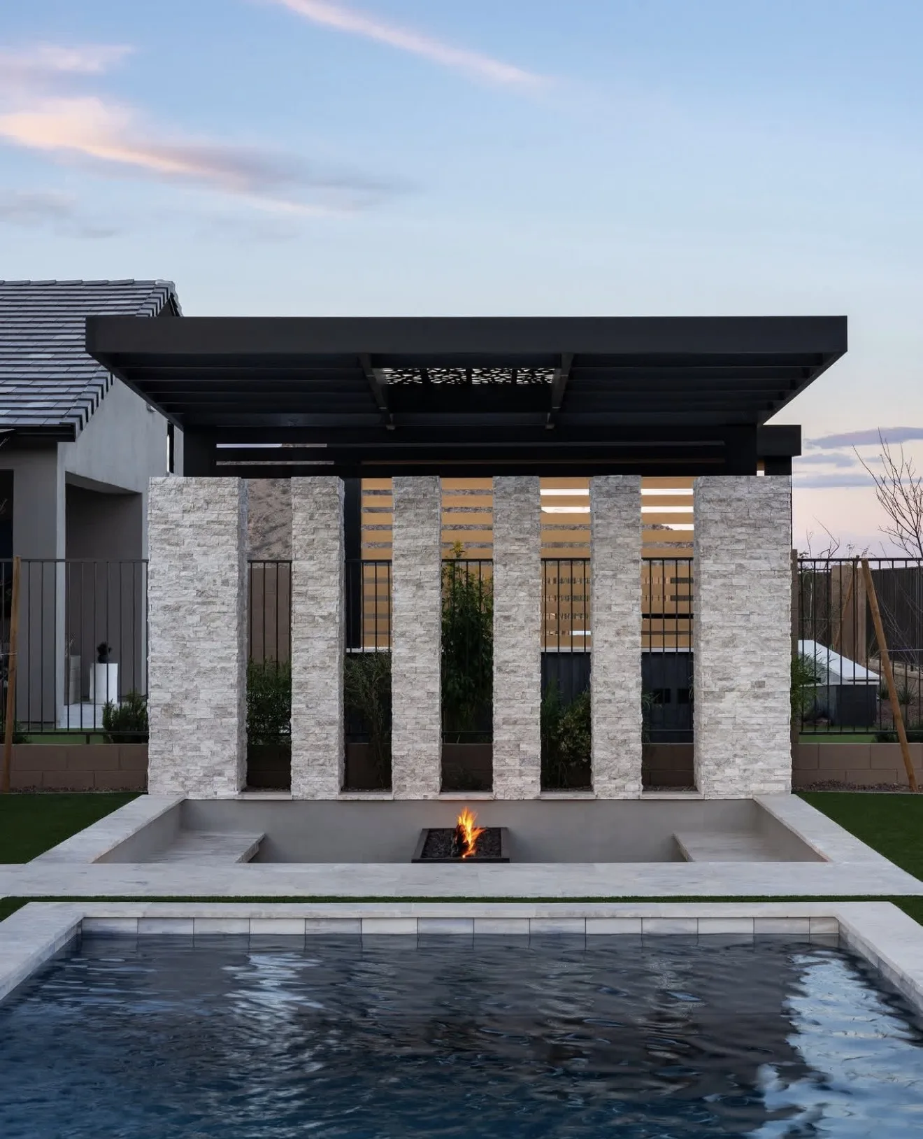 The same stone wall and roof from the lounger side, the fire line running along the sunken terrace at dusk — photograph
