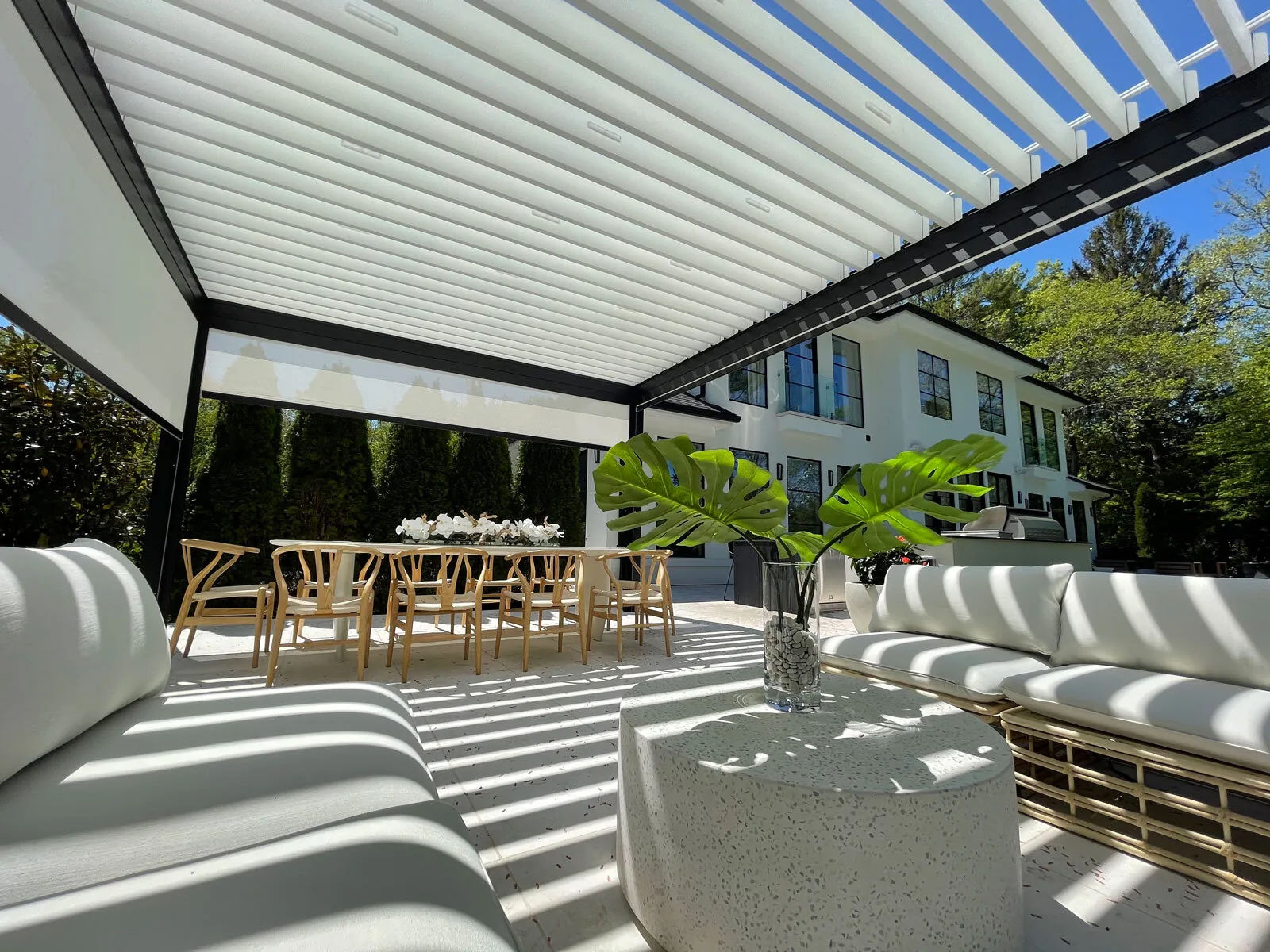From under the same pergola looking out at the house, striped light falling across the seating — photograph