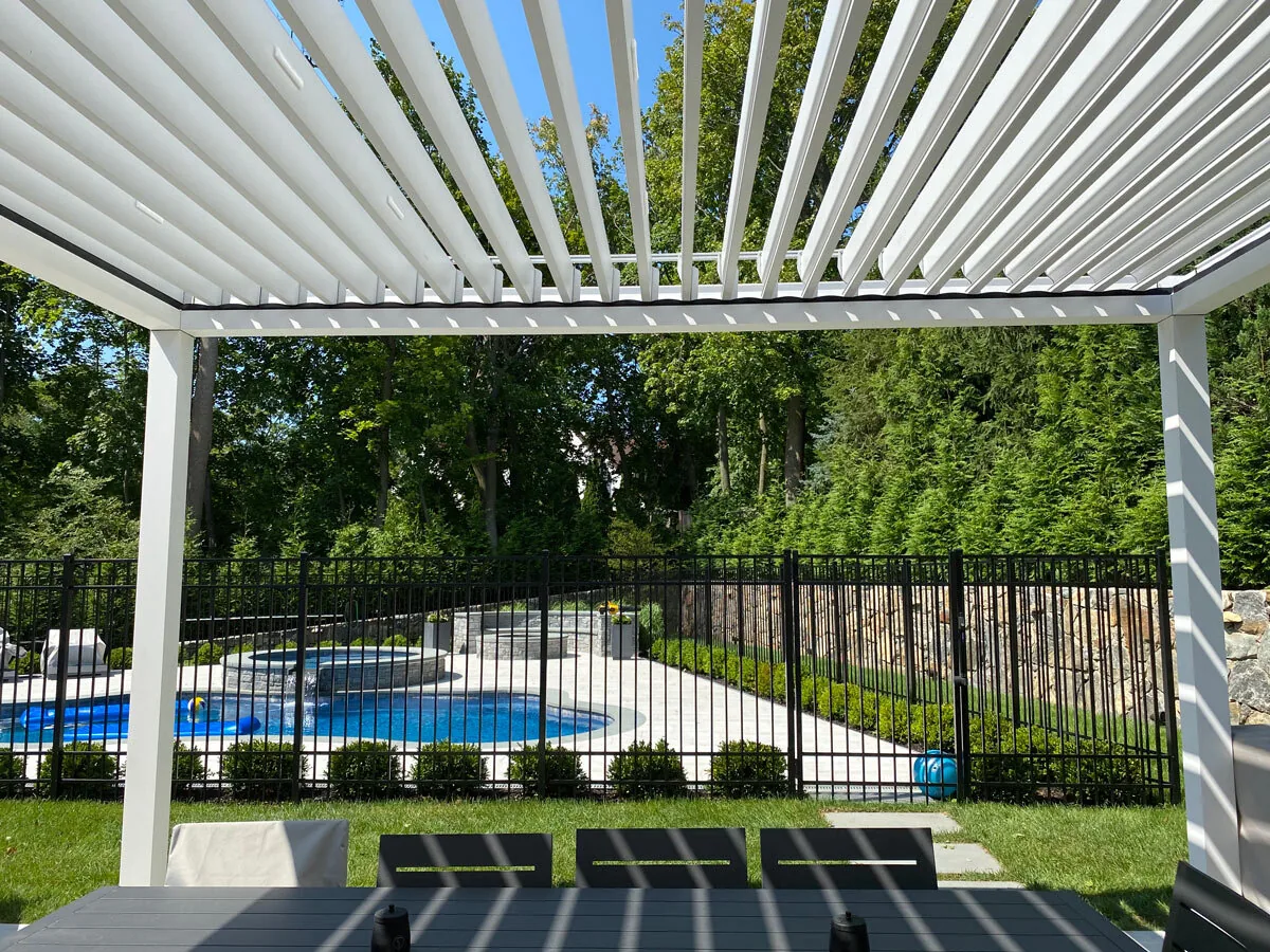 The same roof with its blades turned open, looking out over the pool fence to the water — photograph