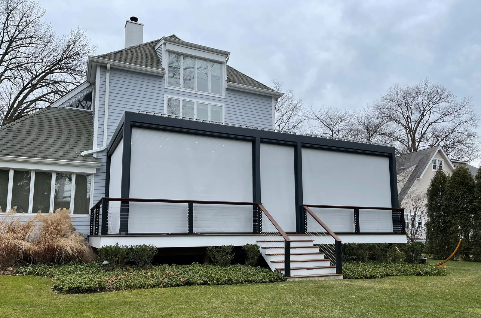 The same deck from the garden with every zip screen lowered, the structure fully enclosed against bare winter trees — photograph