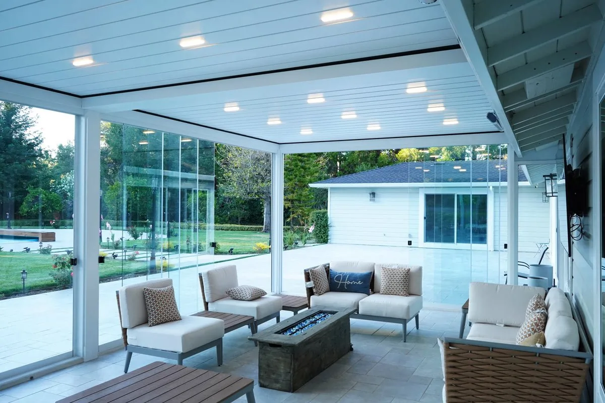 From inside the white pavilion looking out through the sliding glass wall to a pool and lawn beyond — photograph