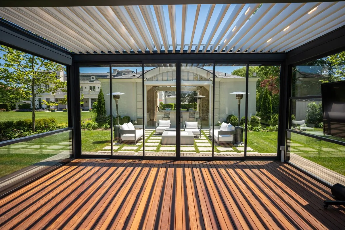 From under the same deck room, a white louvered ceiling above the sliding glass wall, lawn and house beyond — photograph