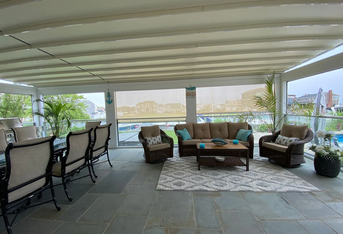From under the same white roof with the zip screens lowered along the water side, dining and lounge seating beneath — photograph